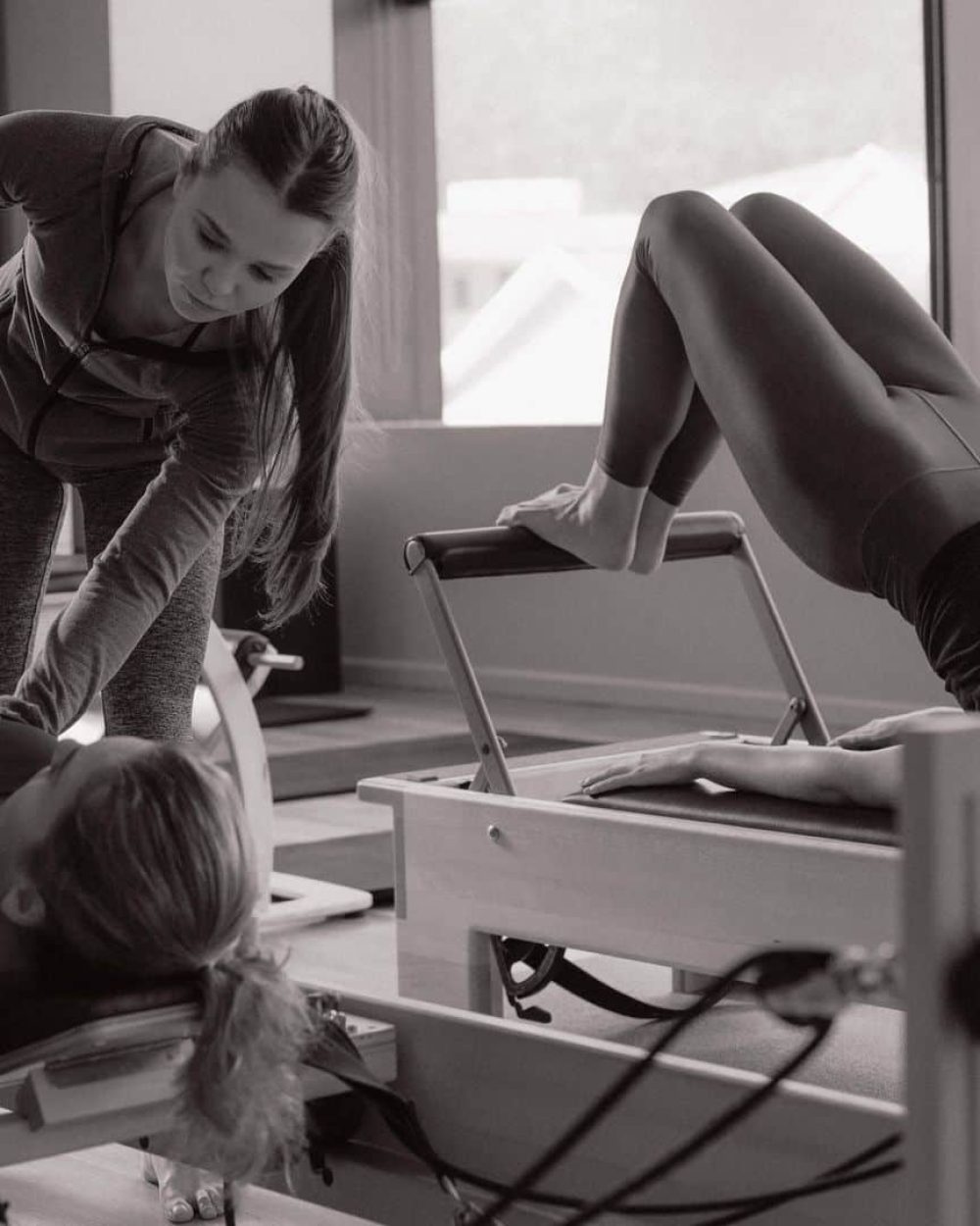 Pilates instructor training women at the gym. Two fitness women doing pilates workout on pilates equipment.