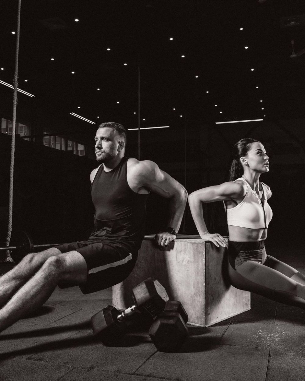 athletic sportsman and sportswoman exercising on cube together in dark gym